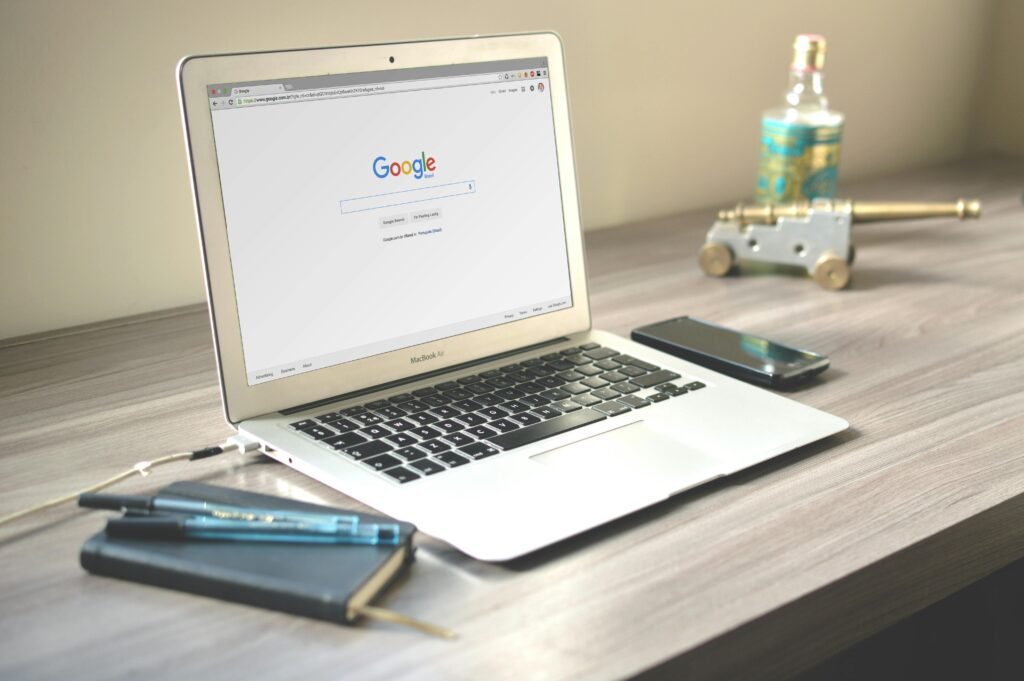 pexels-photo-67112-67112 A neat workspace featuring a laptop displaying Google search, a smartphone, and a notebook on a wooden desk.